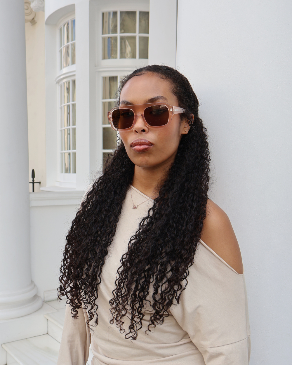 Model wearing Racuzia Yara Transparent Nude 01 sunglasses in front of black door