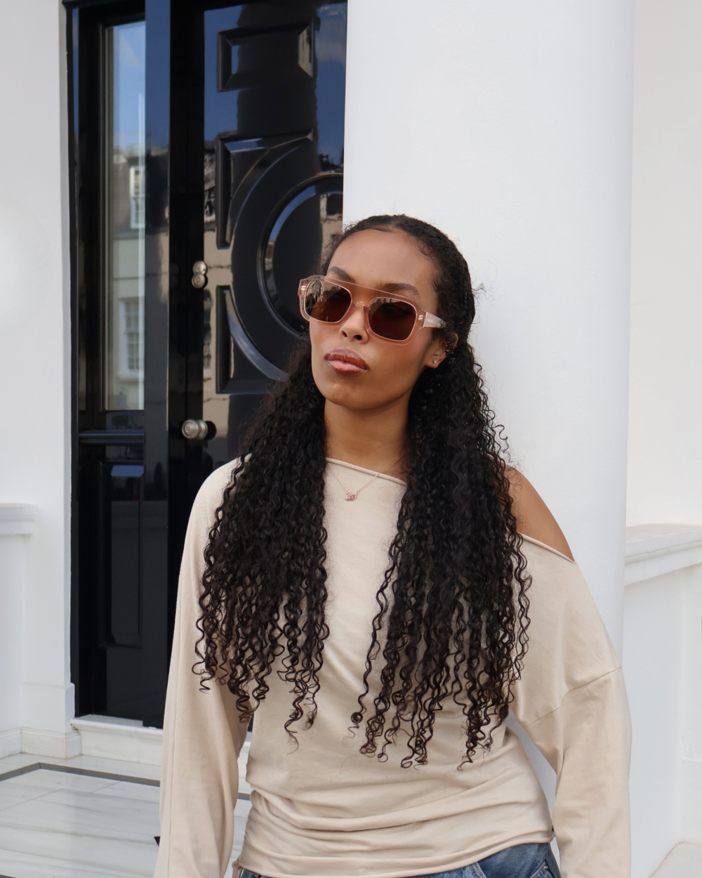 Model wearing Racuzia Yara Transparent Nude 01 sunglasses in front of black door